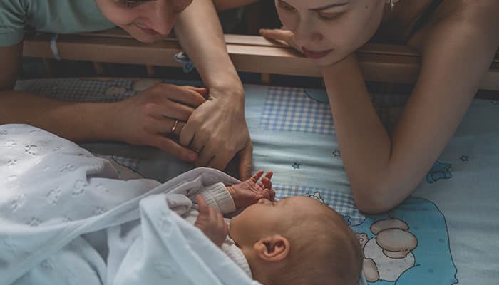 Mother and fatehr watching newborn baby sleep