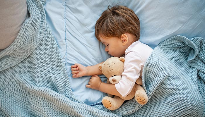 Boy sleeping on bed with teddy bear